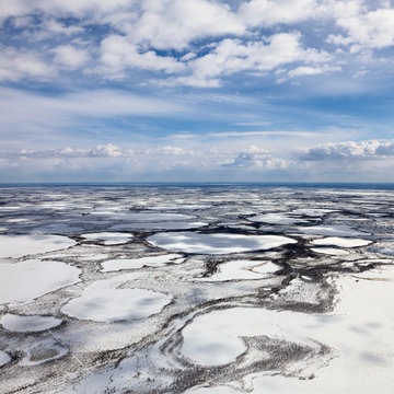 Aerial view above the boundless tundra in winter. Lakes and marshes are covered snow under cloudy sky.