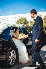 Happy groom helping his bride out of the wedding car.