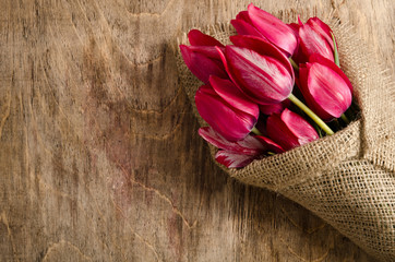 Beautiful bouquet of tulips wrapped in burlap on the wooden tabl