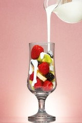Milk/ yogurt pouring over fruits inside smoothie glass.