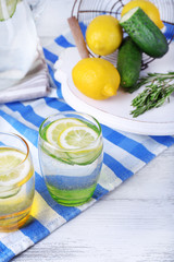 Fresh water with lemon and cucumber in glassware on wooden table, closeup