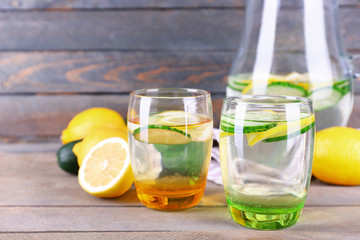 Fresh water with lemon and cucumber in glassware on wooden background