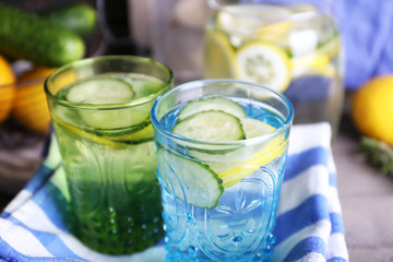 Fresh water with lemon and cucumber in glassware with napkin on wooden table, closeup