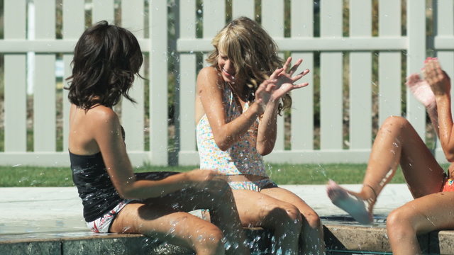 three girls by the pool splashing each other