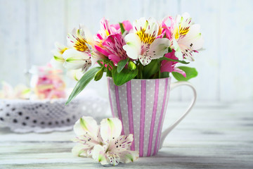 Beautiful flowers in cup, on wooden background