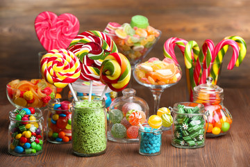 Fototapeta na wymiar Colorful candies in jars on table on wooden background