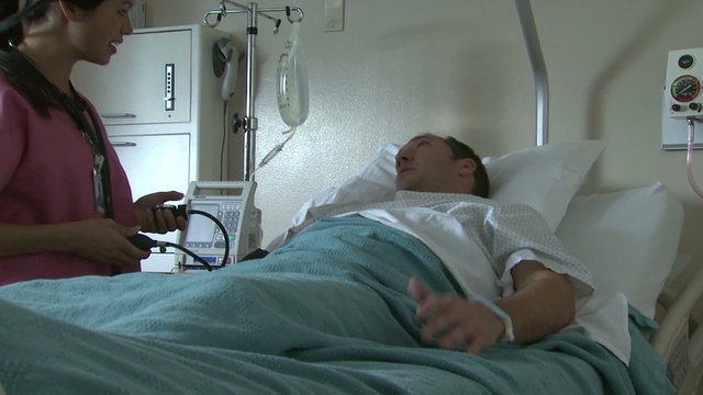 Female nurse taking male patient's blood pressure in hospital bed