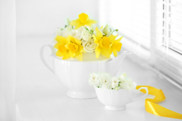 Beautiful bouquet of yellow daffodils and roses in teapot on windowsill