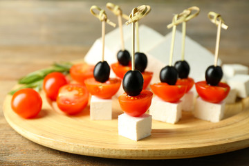 Cheese canapes with cherry tomatoes and olives on wooden tray close up