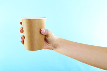 Female hand with paper cup on blue background