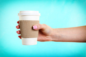 Female hand with paper cup on blue background