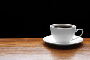 Cup of coffee on wooden table on black background