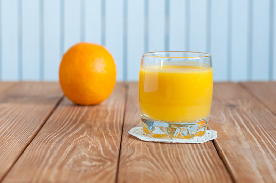 Glass of freshly pressed orange juice with whole fruit on wooden