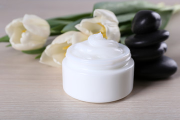Obraz na płótnie Canvas Cosmetic cream with flowers and spa stones on wooden background