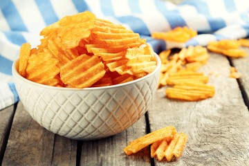 Delicious potato chips in bowl on wooden table close-up