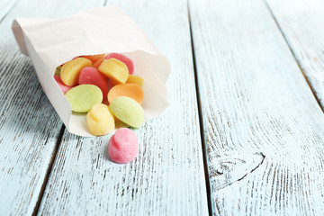 Sweet candies in paper bag on color wooden table, closeup