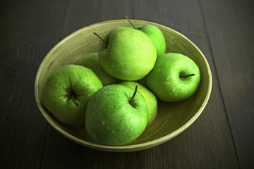 Green apples in bowl on wooden table, closeup