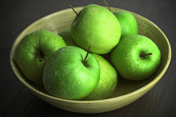 Green apples in bowl on wooden table, closeup