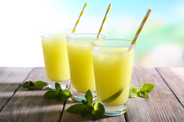 Glasses of cocktails on wooden table on bright blurred background