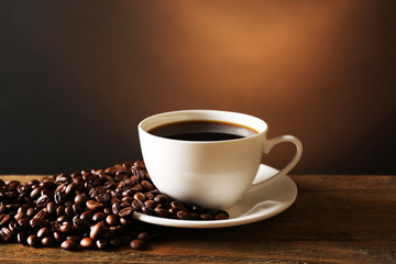 Cup of coffee with grains on wooden table on dark background