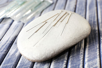 Acupuncture needles on wooden table with spa stones, closeup