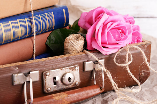 Beautiful pink roses with stack of books in suitcase, closeup