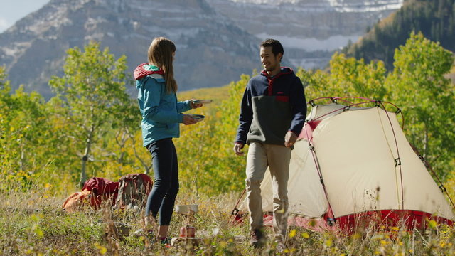 Wide panning shot of couple kissing with food cooked on camping stove / American Fork Canyon, Utah, United States