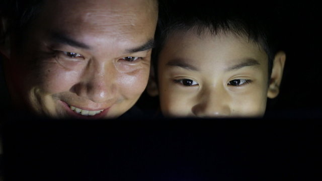 Father and son are looking at the laptop in the bedroom