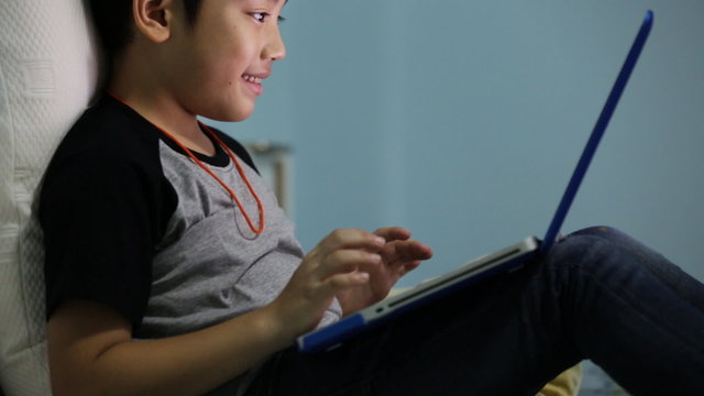 Asian cute boy watching and talking on laptop computer.
