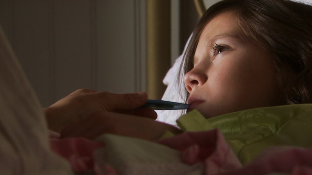 Girl in bed with thermometer in mouth and mother