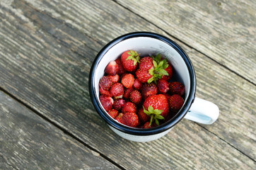 Wild strawberry in enamel cup on wooden table