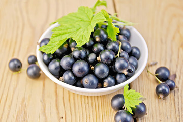 Black currants in bowl with leaf on board