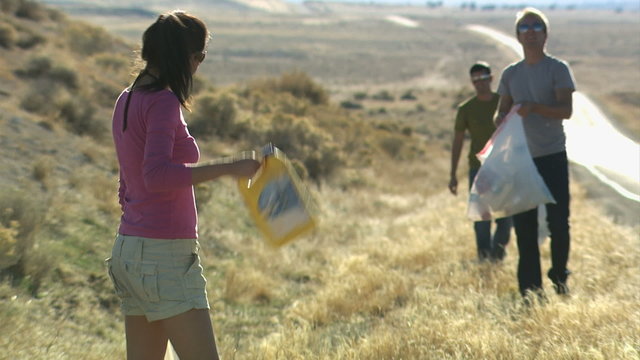 three people picking up trash on the side of the road