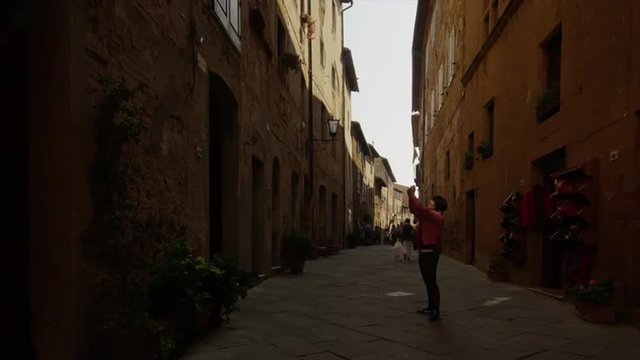 Medium shot of tourist taking photographs in Italian alley / Piensa, Tuscany, Italy