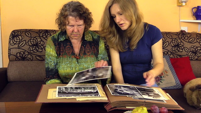 Happy granddaughter woman with senior grandmother look at photos