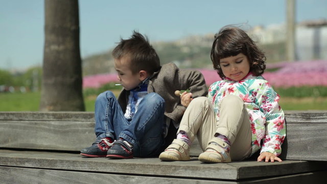 Two children are sitting on wooden stairs and eat candy sti