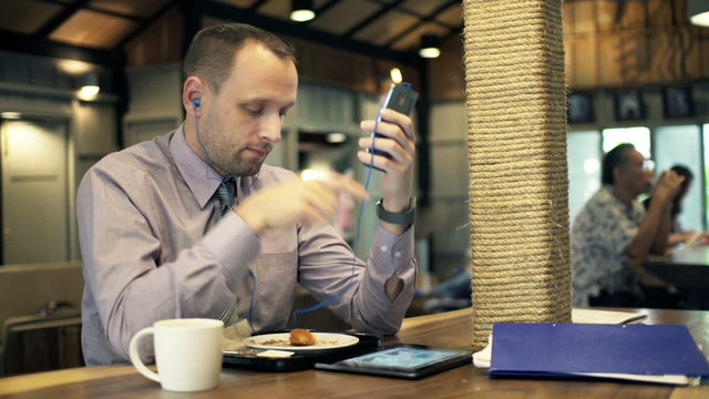 Young businessman listening to music, drinking in cafe