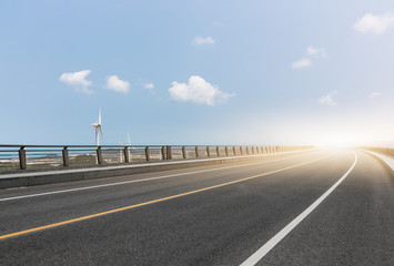Fototapeta premium Wind turbines on landscape along empty road against sky