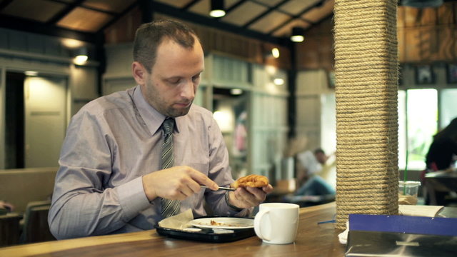 Young businessman slicing tasty croissant with knife in cafe 
