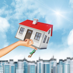 House and keys in womans hand with cityscape