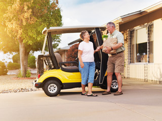 active senior couple coming home with groceries on golf cart