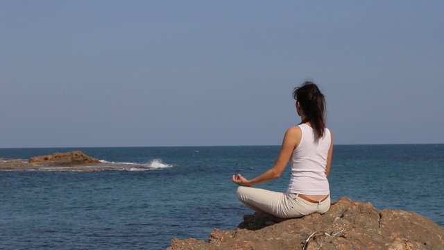 Young woman meditating in lotus position near the sea
