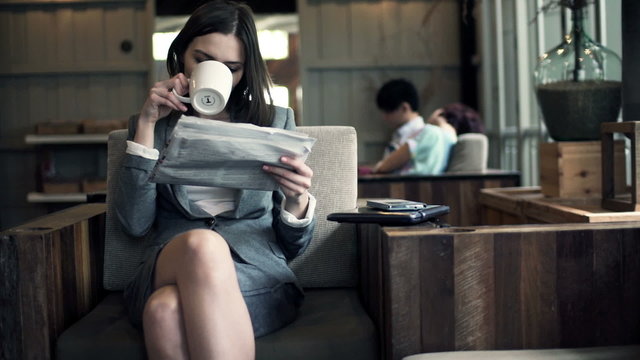 businesswoman reading newspaper and drinking coffee in cafe
