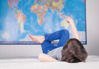 Boy lying on sofa and studying map of world