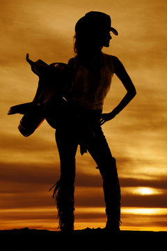 silhouette of a cowgirl hold saddle on shoulder look to side
