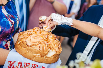 Groom holding slice of traditional wedding round loaf and bride