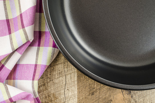 Folded tablecloth and frying pan on white wooden background