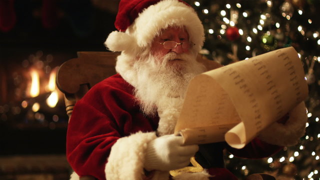 Santa Claus reading his naughty and nice list in a chair by the fire