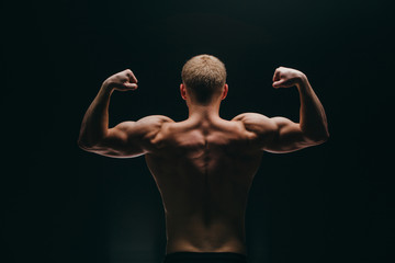muscular young man showing his biceps isolated on black - obrazy, fototapety, plakaty
