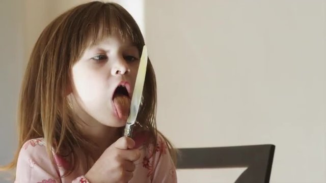 CU Girl (4-5) licking knife in kitchen / Cedar Hills, Utah, USA